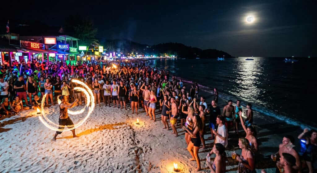 Crowds and fire dancers on Haad Rin Beach during the Full Moon Party in Koh Phangan, Thailand at night